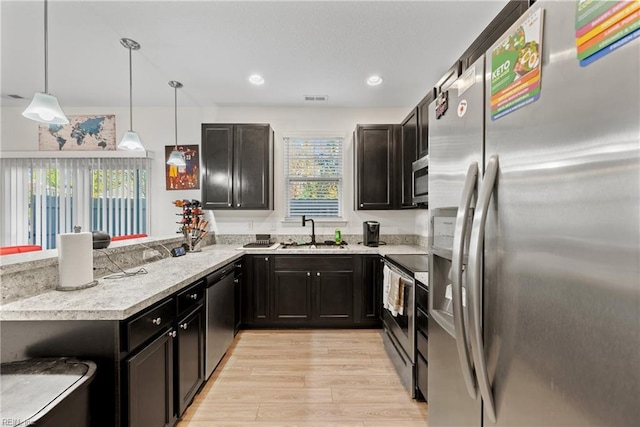 kitchen featuring stainless steel appliances, sink, decorative light fixtures, light hardwood / wood-style floors, and kitchen peninsula