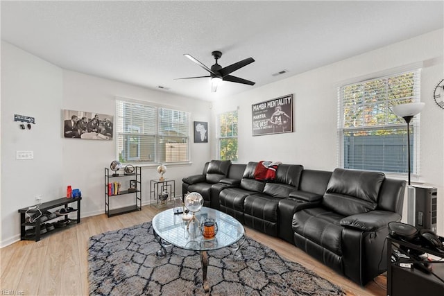 living room featuring light wood-type flooring, ceiling fan, and a textured ceiling