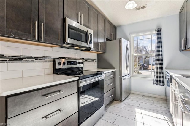 kitchen featuring appliances with stainless steel finishes, a textured ceiling, tasteful backsplash, and dark brown cabinetry