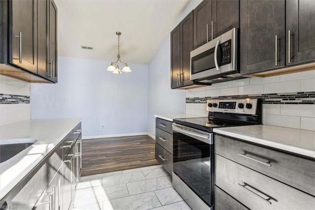 kitchen featuring appliances with stainless steel finishes, decorative backsplash, dark brown cabinets, an inviting chandelier, and decorative light fixtures