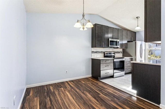 kitchen with vaulted ceiling, light hardwood / wood-style floors, stainless steel appliances, decorative backsplash, and decorative light fixtures