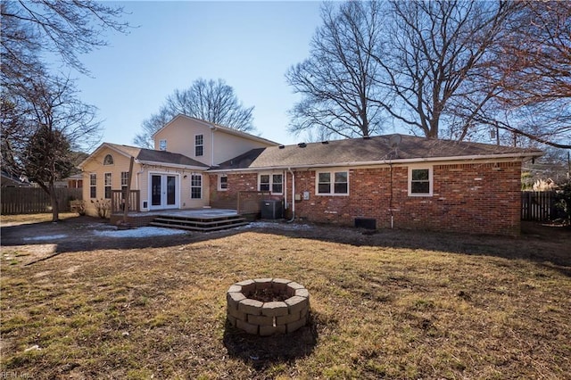 rear view of house with french doors, a deck, a lawn, and a fire pit