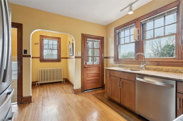 kitchen featuring sink, light hardwood / wood-style floors, radiator heating unit, plenty of natural light, and appliances with stainless steel finishes