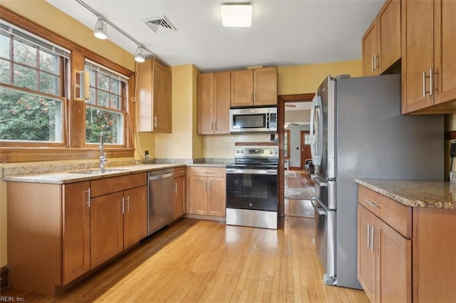 kitchen with appliances with stainless steel finishes, light hardwood / wood-style floors, light stone countertops, and sink