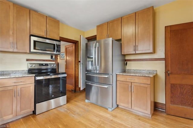 kitchen with light stone counters, appliances with stainless steel finishes, and light hardwood / wood-style flooring