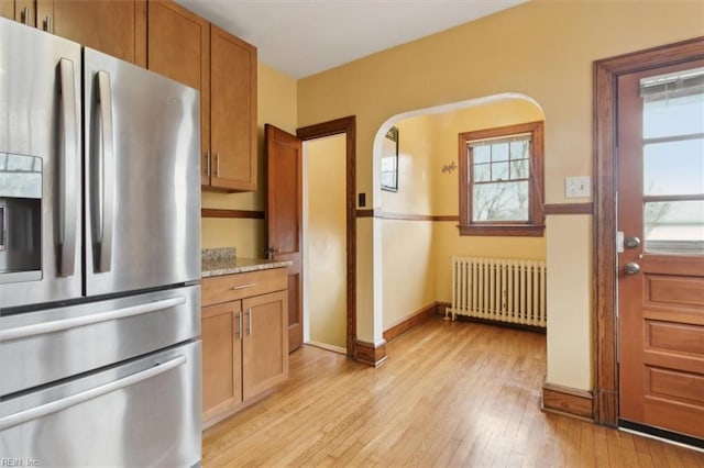 kitchen featuring light stone countertops, light hardwood / wood-style floors, radiator, and stainless steel refrigerator with ice dispenser