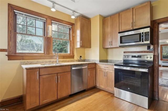 kitchen featuring sink, light hardwood / wood-style floors, light stone counters, and appliances with stainless steel finishes