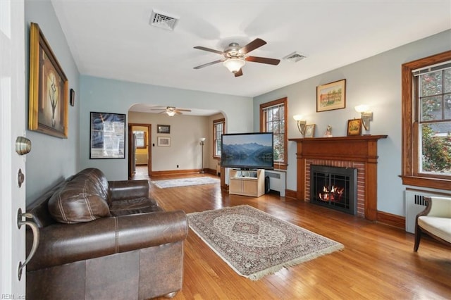 living room with a fireplace, ceiling fan, light hardwood / wood-style floors, and radiator