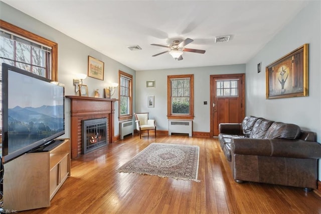 living room with ceiling fan, light wood-type flooring, a brick fireplace, and radiator heating unit