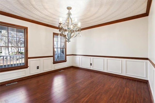 spare room featuring dark hardwood / wood-style floors, an inviting chandelier, crown molding, and plenty of natural light