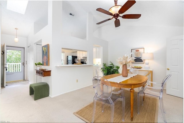 dining space with ceiling fan, light carpet, and vaulted ceiling with skylight