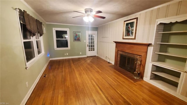 unfurnished living room featuring hardwood / wood-style floors, ornamental molding, ceiling fan, a brick fireplace, and built in shelves