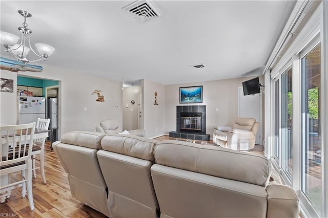 living room with light wood-type flooring, a wealth of natural light, a fireplace, and a notable chandelier