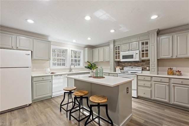 kitchen with white appliances, light hardwood / wood-style floors, a kitchen island, a breakfast bar area, and sink