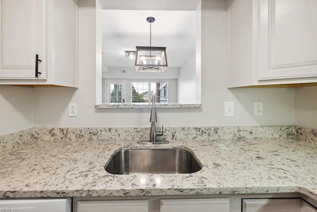 kitchen with white cabinetry, light stone counters, and sink