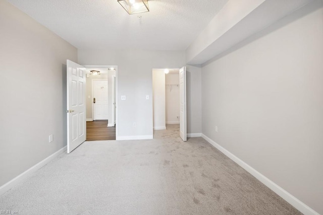 unfurnished bedroom with carpet, a closet, a walk in closet, and a textured ceiling