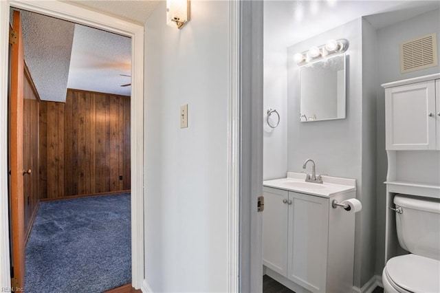 bathroom with a textured ceiling, toilet, wood walls, and vanity