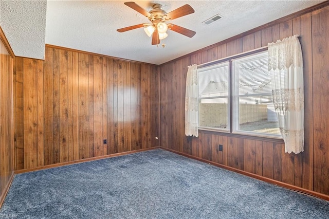 unfurnished room featuring ceiling fan, dark carpet, wood walls, and a textured ceiling