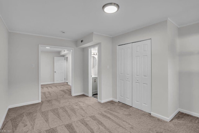 unfurnished bedroom featuring ensuite bathroom, light colored carpet, a closet, and crown molding