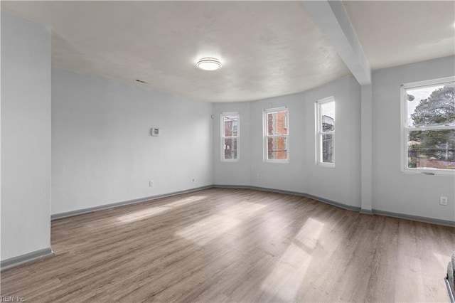 unfurnished room featuring a healthy amount of sunlight, beam ceiling, and wood-type flooring