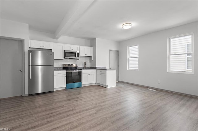 kitchen with appliances with stainless steel finishes, wood-type flooring, beam ceiling, and white cabinets