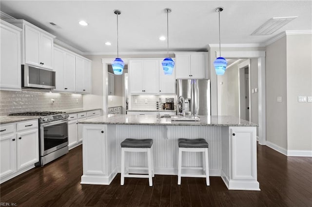 kitchen featuring white cabinets, stainless steel appliances, decorative light fixtures, and a center island with sink