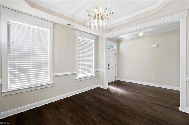 empty room featuring dark hardwood / wood-style flooring, a raised ceiling, an inviting chandelier, and crown molding