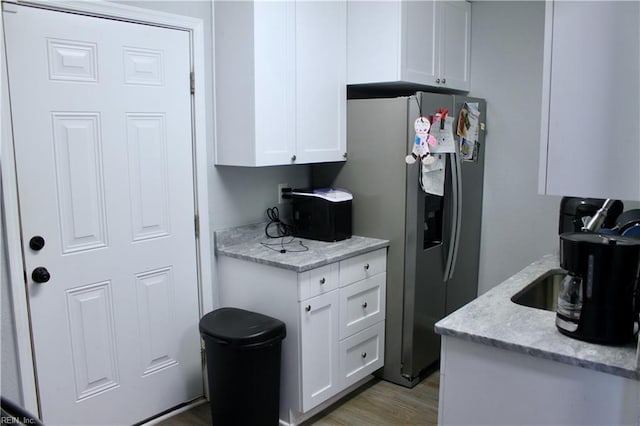 kitchen with light wood-type flooring, stainless steel refrigerator with ice dispenser, light stone counters, and white cabinetry