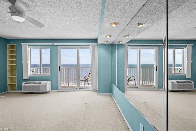 carpeted empty room with an AC wall unit, ceiling fan, and a water view