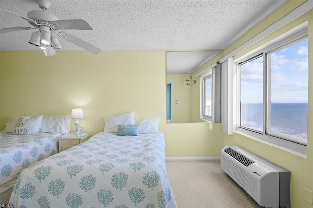 bedroom with light colored carpet, a water view, ceiling fan, a wall mounted air conditioner, and a textured ceiling