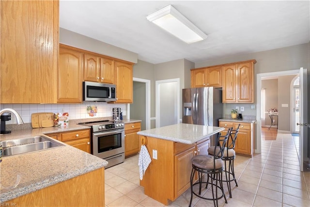 kitchen with a center island, stainless steel appliances, a breakfast bar, decorative backsplash, and sink