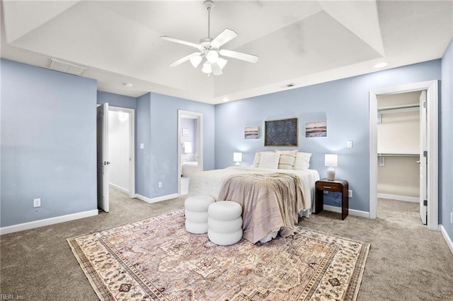 bedroom featuring a raised ceiling, ensuite bath, and ceiling fan