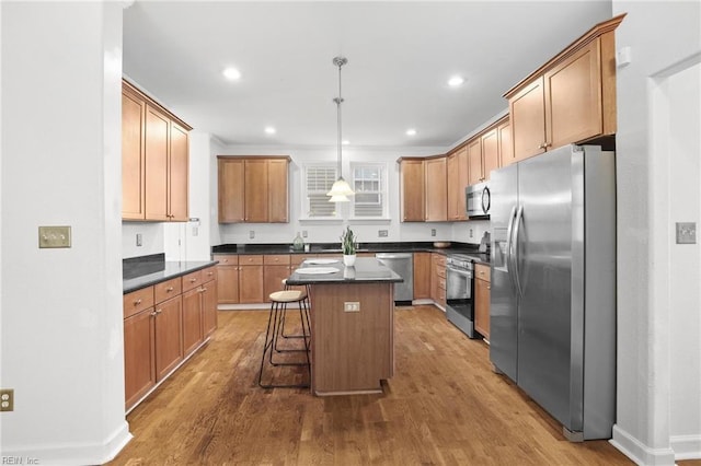 kitchen with hardwood / wood-style flooring, appliances with stainless steel finishes, a kitchen breakfast bar, hanging light fixtures, and a kitchen island