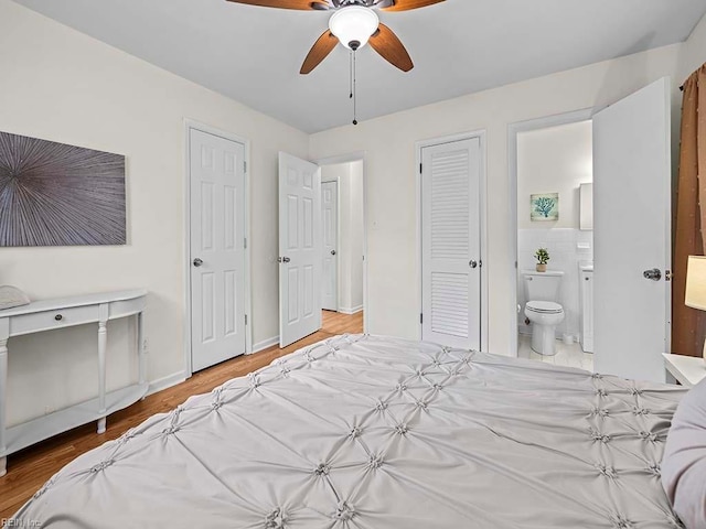 bedroom featuring ceiling fan, ensuite bathroom, wood-type flooring, and multiple closets