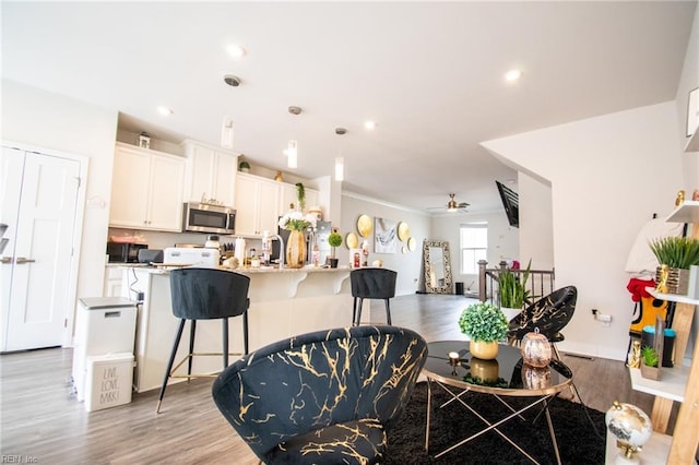 kitchen with a breakfast bar area, hanging light fixtures, ceiling fan, light stone counters, and white cabinetry