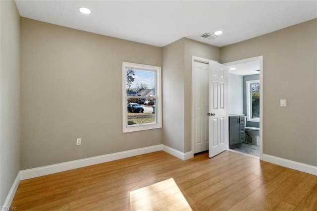 unfurnished bedroom featuring ensuite bathroom and light wood-type flooring