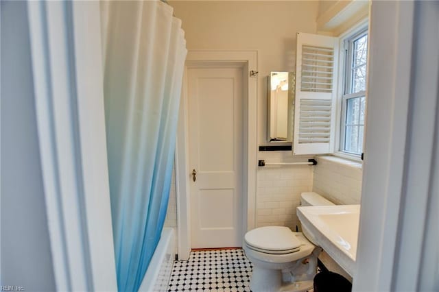 bathroom with toilet, tile walls, and shower / bath combination with curtain