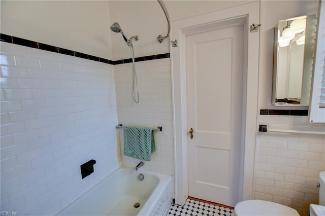 bathroom with toilet, tiled shower / bath, and tile walls