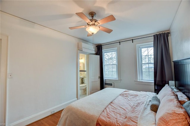 bedroom featuring hardwood / wood-style floors, radiator heating unit, a wall unit AC, ceiling fan, and ensuite bathroom