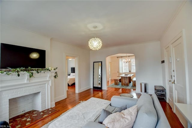 living room with hardwood / wood-style flooring, ornamental molding, a brick fireplace, and a chandelier