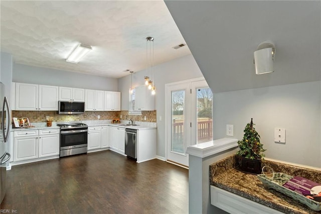 kitchen featuring kitchen peninsula, appliances with stainless steel finishes, dark stone counters, pendant lighting, and white cabinets