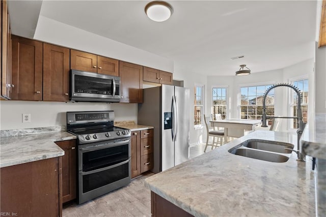 kitchen with light stone counters, sink, stainless steel appliances, and light wood-type flooring