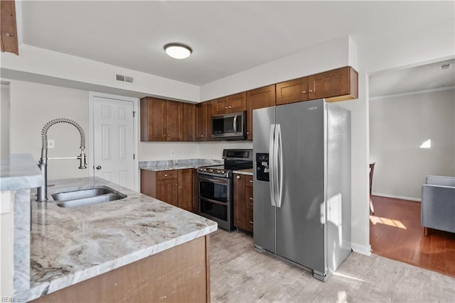 kitchen with light stone countertops, sink, stainless steel appliances, and light wood-type flooring