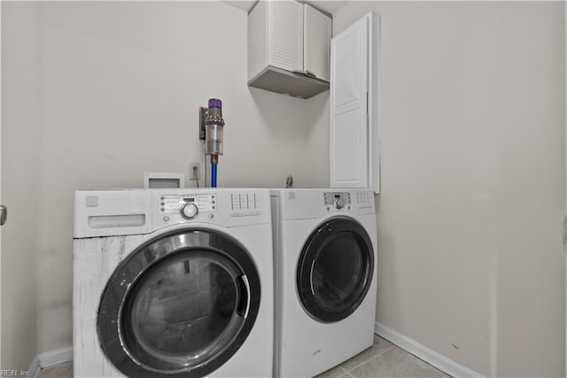 clothes washing area with cabinets, light tile patterned floors, and washer and clothes dryer