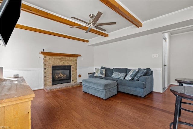 living room with ceiling fan, a brick fireplace, beam ceiling, ornamental molding, and dark hardwood / wood-style flooring