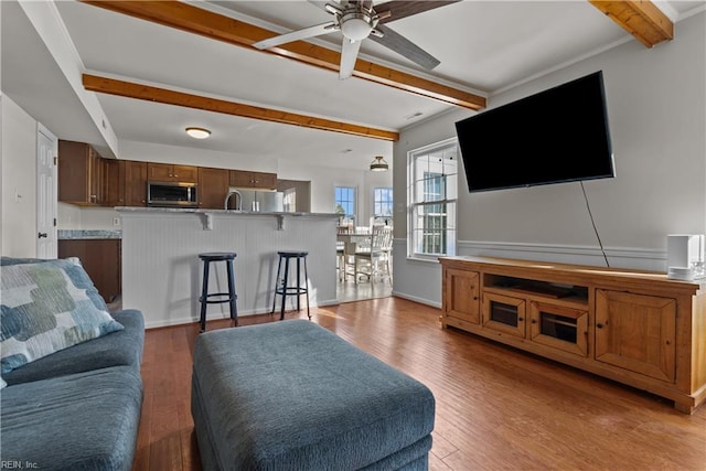 living room with ceiling fan, beamed ceiling, and light wood-type flooring