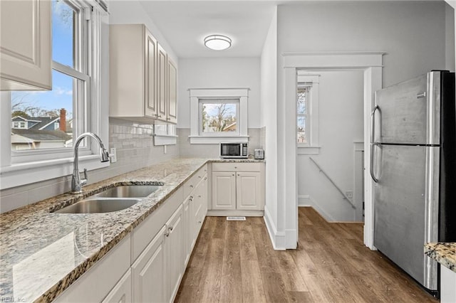 kitchen with appliances with stainless steel finishes, sink, white cabinets, decorative backsplash, and light stone countertops