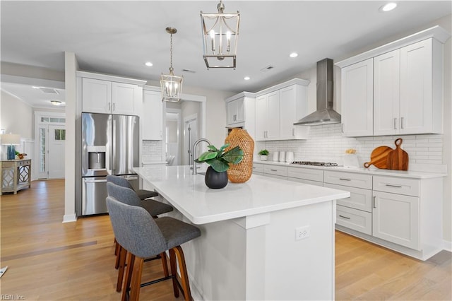 kitchen featuring white cabinetry, wall chimney range hood, a center island with sink, and stainless steel appliances