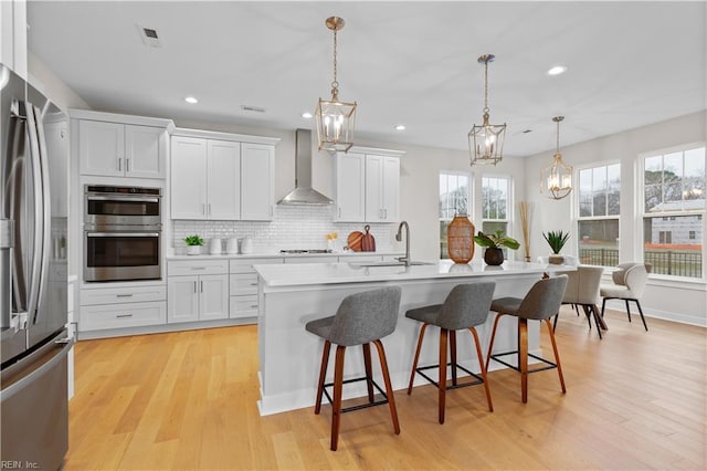 kitchen with stainless steel appliances, hanging light fixtures, wall chimney range hood, white cabinets, and sink