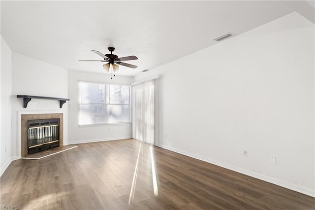 unfurnished living room with ceiling fan, a tiled fireplace, and dark wood-type flooring